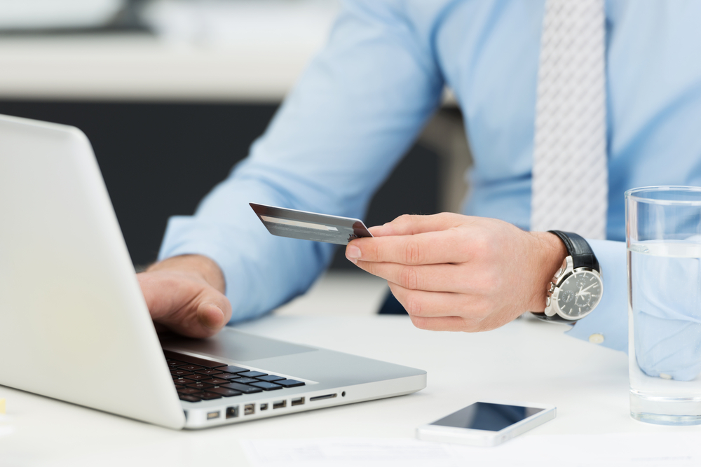 Businessman doing online banking, making a payment or purchasing goods on the internet entering his credit card details on a laptop, close up view of his hands Businessman doing online banking, making a payment or purchasing goods on the internet entering his credit card details on a laptop, close up view of his hands